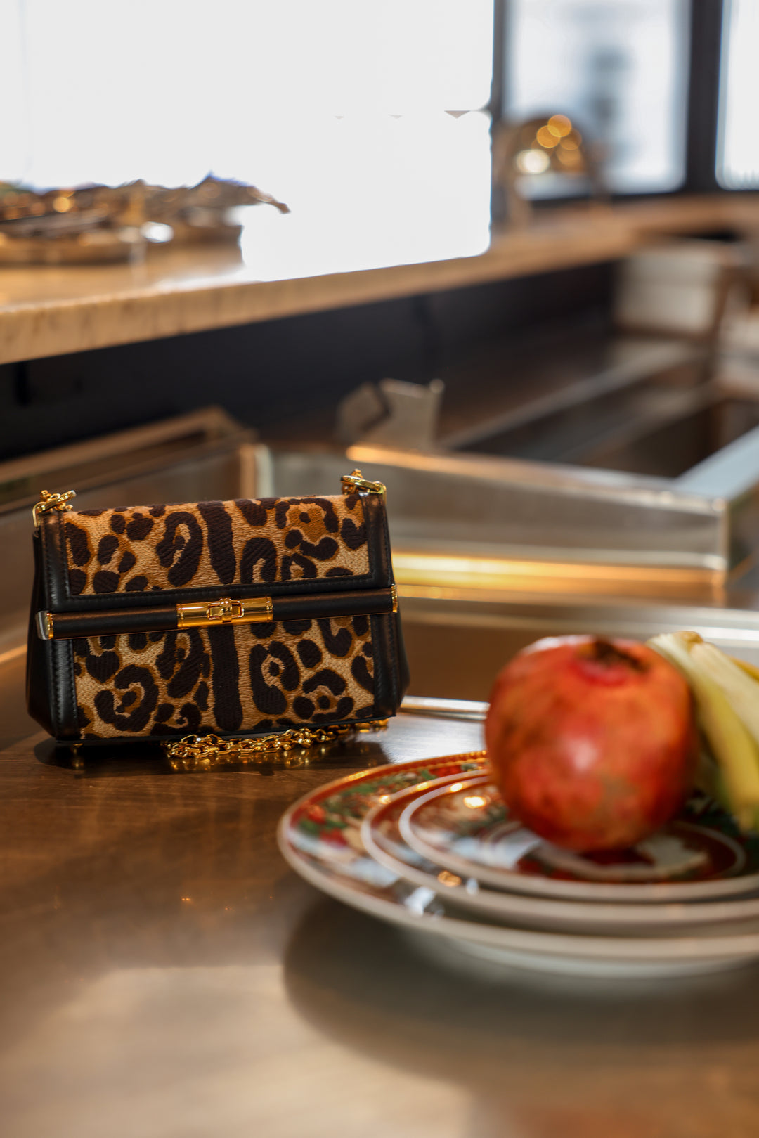 Leopard print handbag on a kitchen counter with fruit and plates.